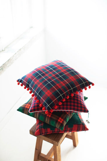 Festive tartan plaid pillow with pom-poms styled in a cozy holiday-themed living room