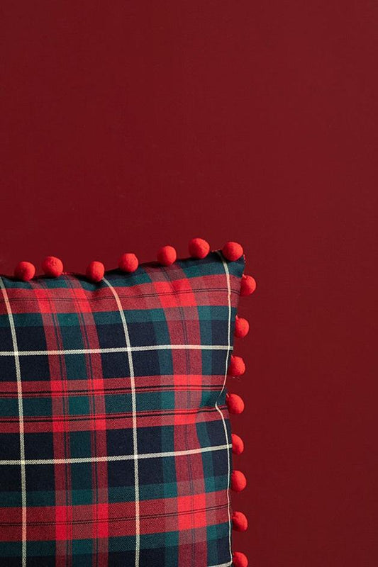 Close-up of red pom-pom edges and checkered tartan plaid fabric for the festive pillow cover