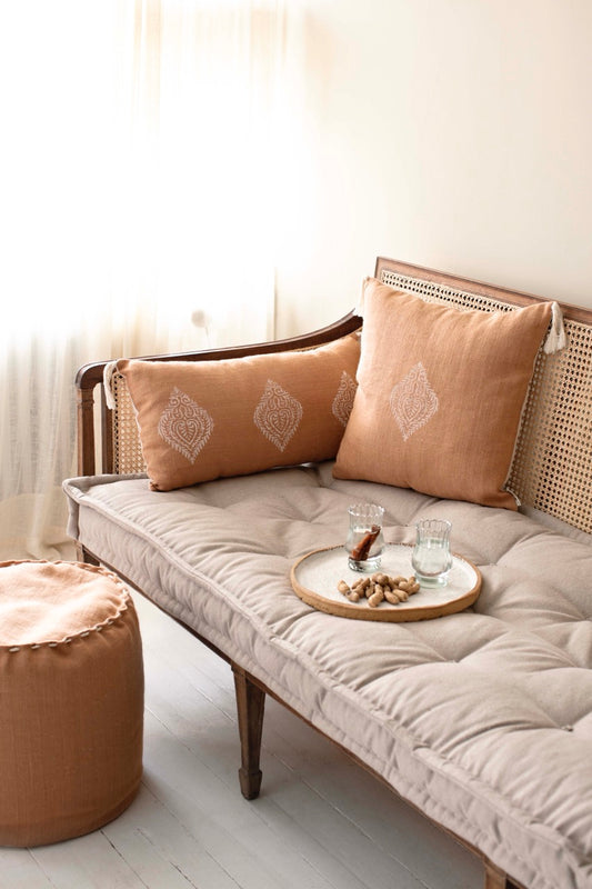 Tile-colored square and rectangular block print cushions with tassels on wooden sofa in a sunlit living room.