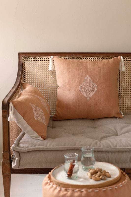 Two handmade tile colored block print cushion covers with tassels placed on a wooden sofa in a cozy living room setting