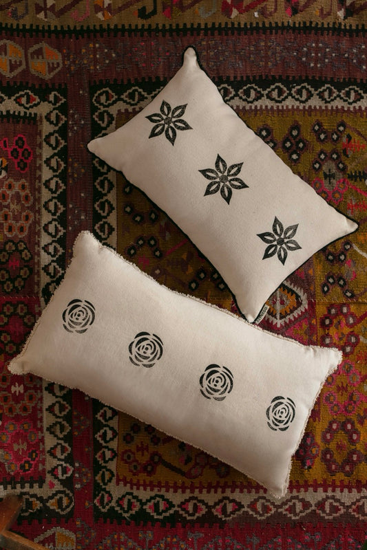 Beige blockprint pillows with black star and rose motifs on traditional kilim rug